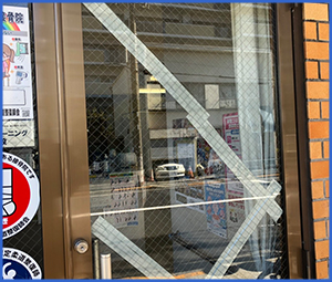 店舗のガラスに大きく入ったヒビに白いガムテを貼っている画像