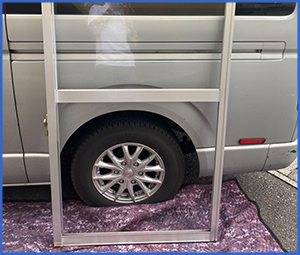 車の前に立てかけたガラスが抜けた窓枠画像